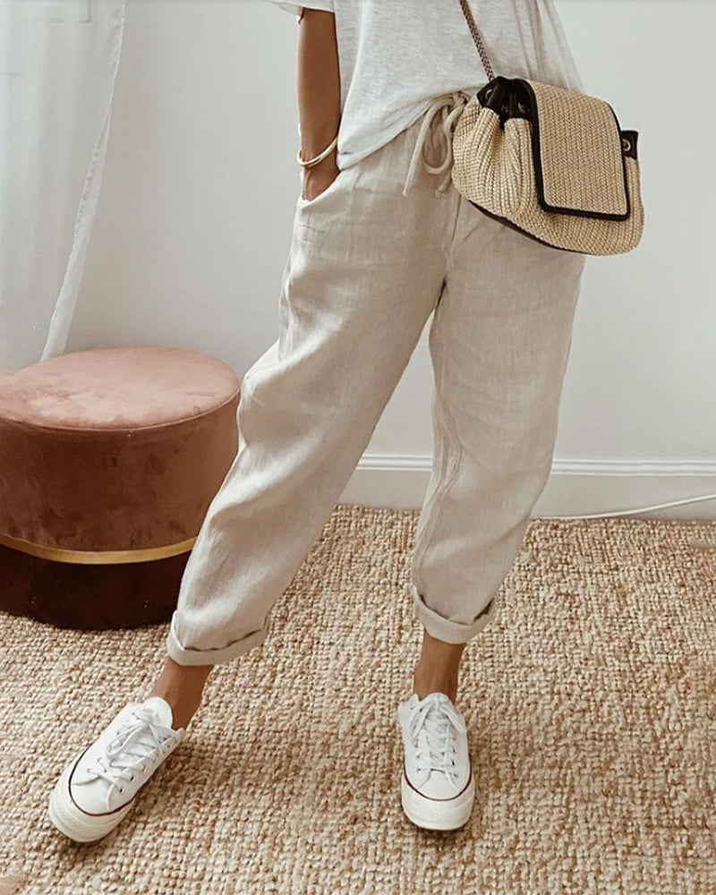 Pantalon fluide beige Danoir Paris, confortable et élégant, en tissu léger, porté de côté avec ceinture ajustable.