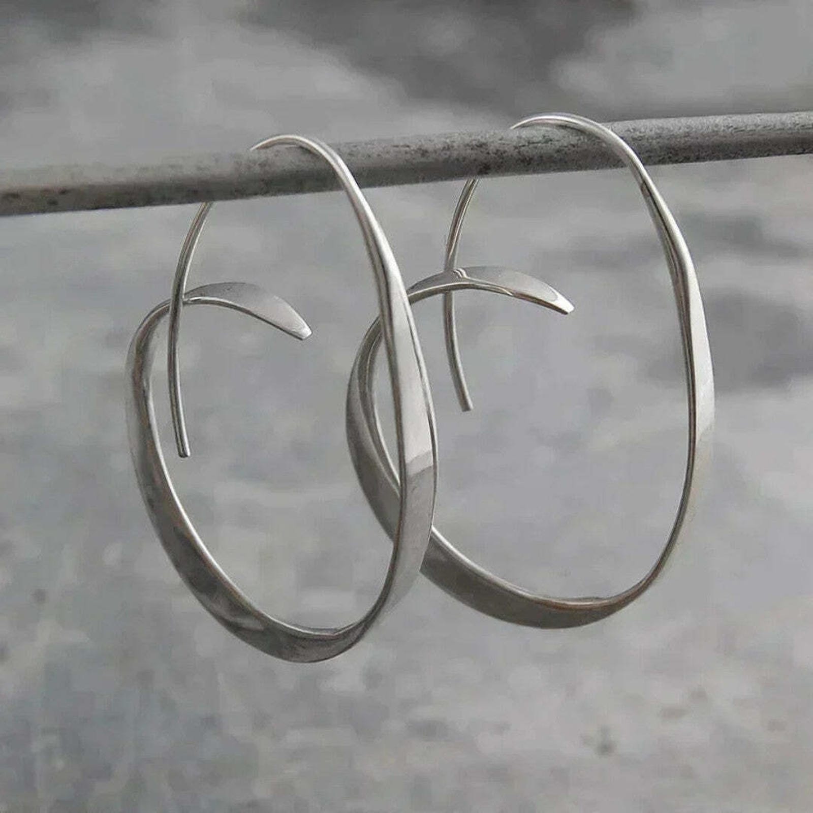 Boucles d'oreilles pendantes en spirale ouverte en argent par Danoir Paris, visibles avec détails de la finition métallique.