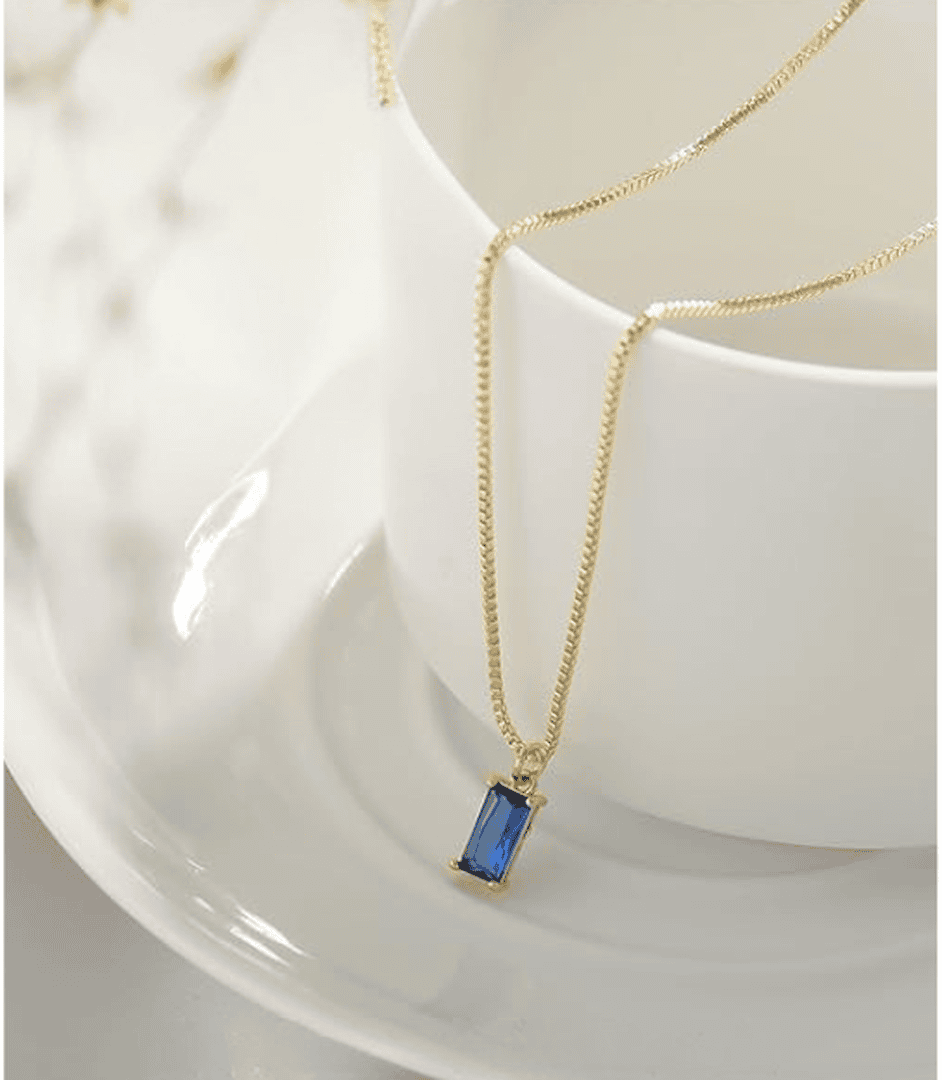 Collier minimaliste en saphir de Danoir Paris avec pendentif élégant, porté sur un fond neutre.