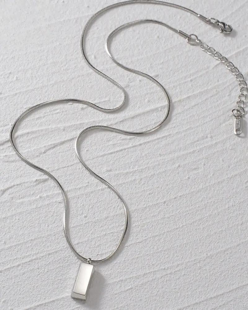 Pendentif Axis Tag de la marque Old Money avec un design minimaliste en métal argenté, suspendu à une chaîne fine.