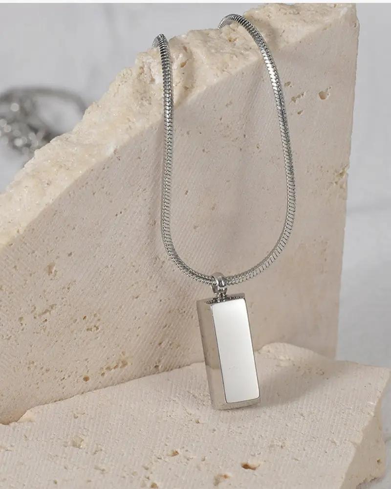 Pendentif Axis Tag de la marque Old Money avec un design élégant en métal argenté et une étiquette gravée.